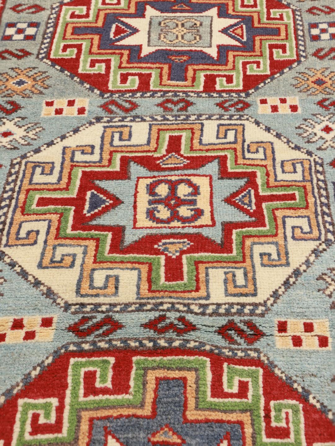 Een handgeknoopt Kazak-tapijt uit Afghanistan met blauwe en rode geometrische patronen.