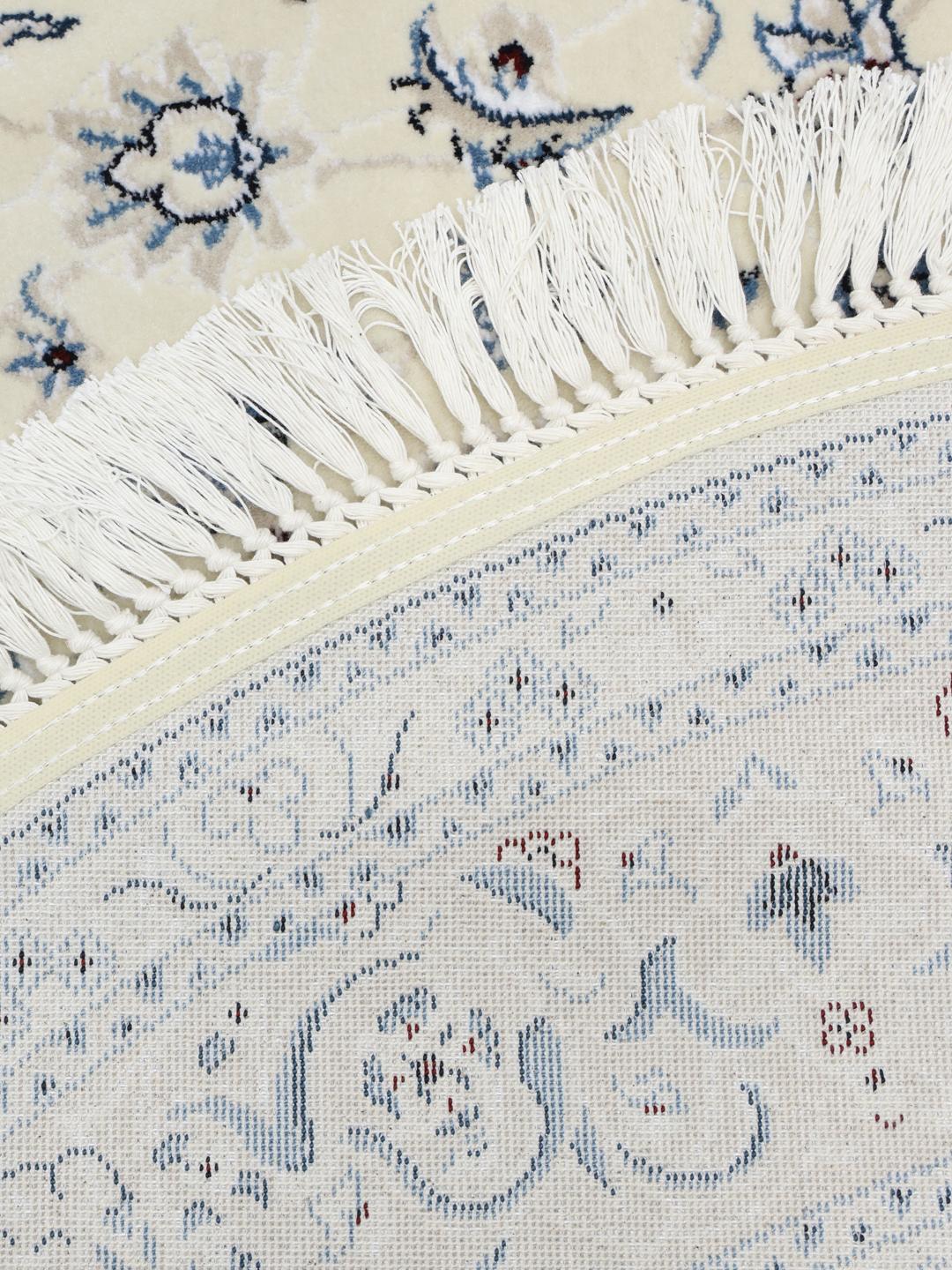 Rundt tæppe i beige og lyseblå med detaljerede blomstermotiver og frynsekant.