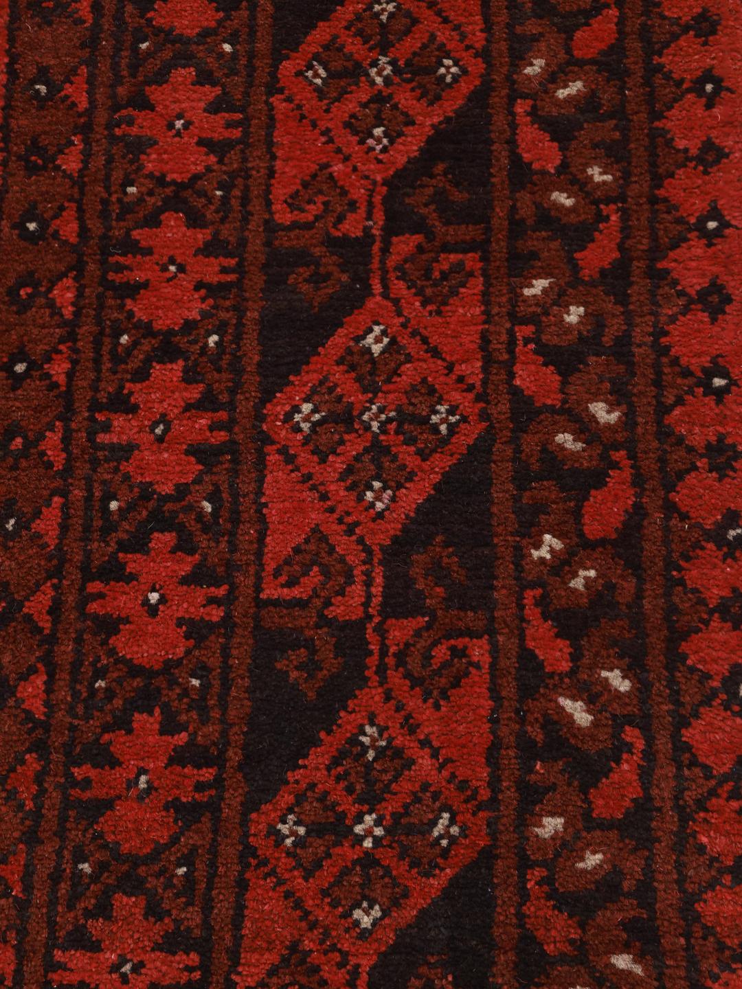 Et håndknyttet afghansk tæppe med en dybrød bund og traditionelle geometriske mønstre.