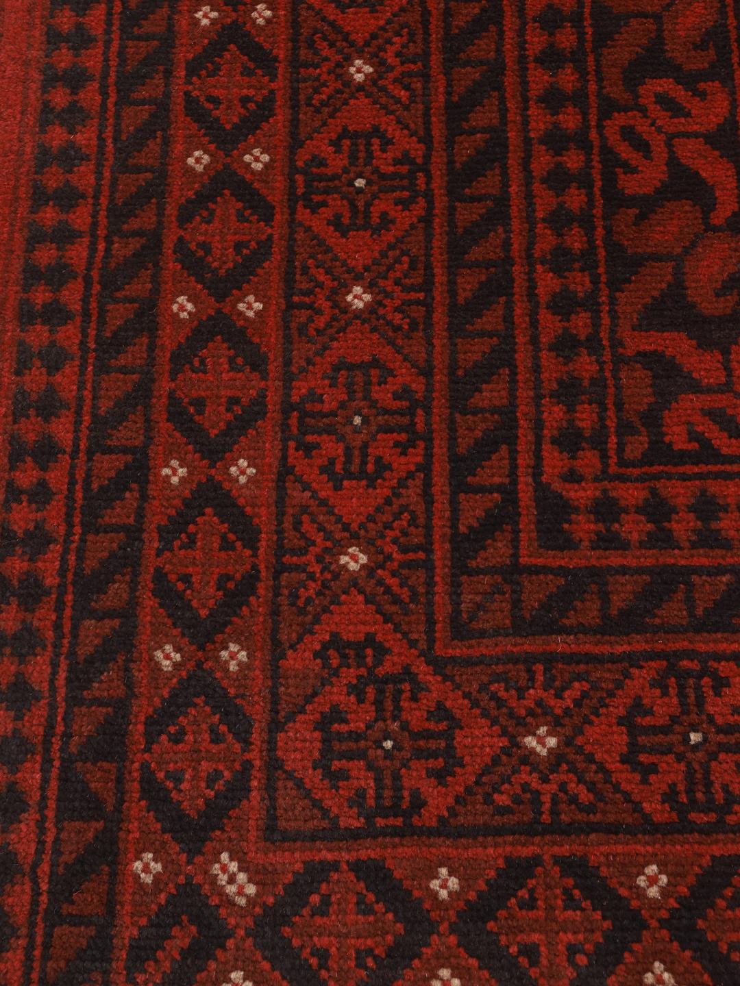 Håndknyttet afghansk tæppe med en dyb rød flade og komplekse geometriske kanter