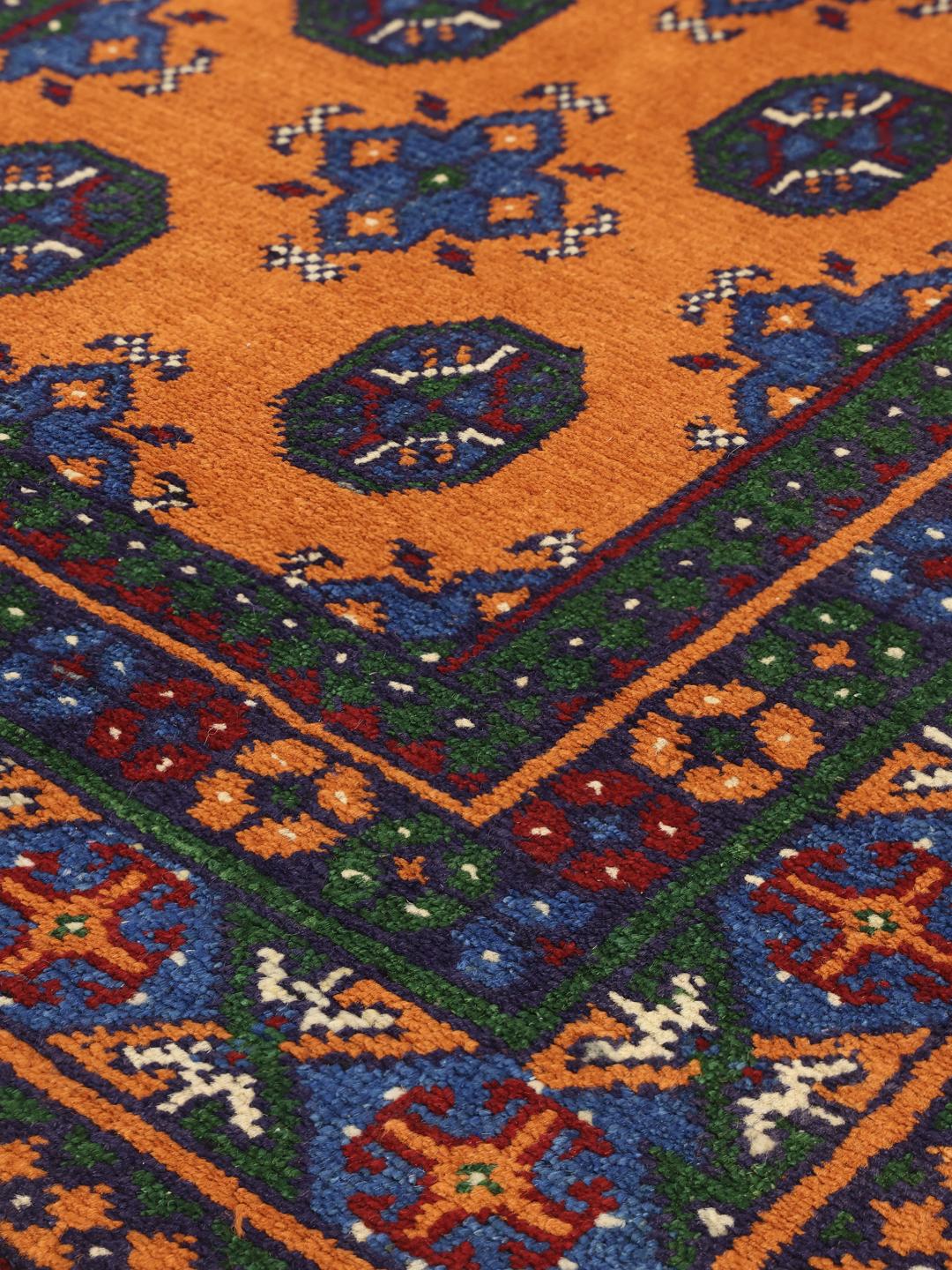 Hand-knotted Afghan rug with vibrant orange, blue, and green geometric tribal patterns.