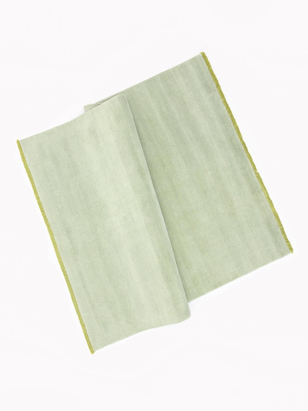 Een handgeweven tapijt in een zachte mintgroene kleur met decoratieve franjes.