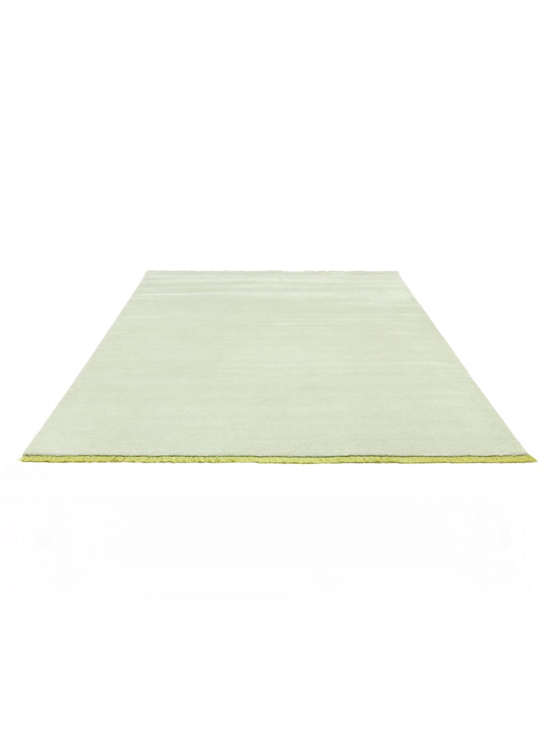 Een handgeweven tapijt in een zachte mintgroene kleur met decoratieve franjes.