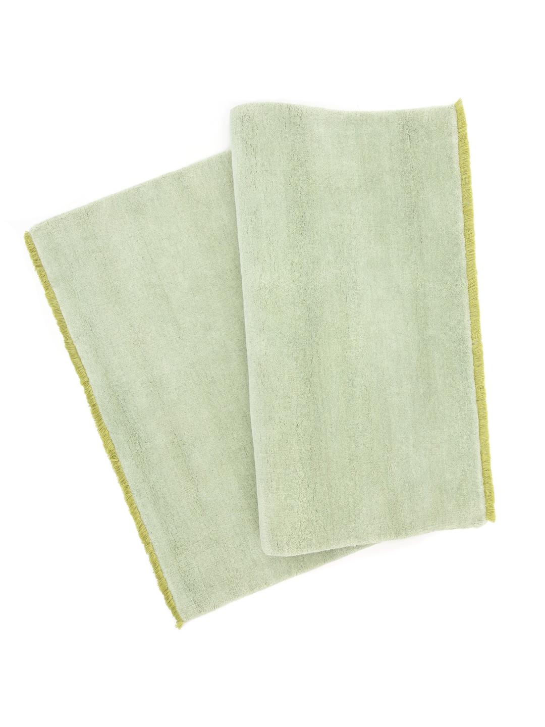 Een handgeweven tapijt in een zachte mintgroene kleur met decoratieve franjes.