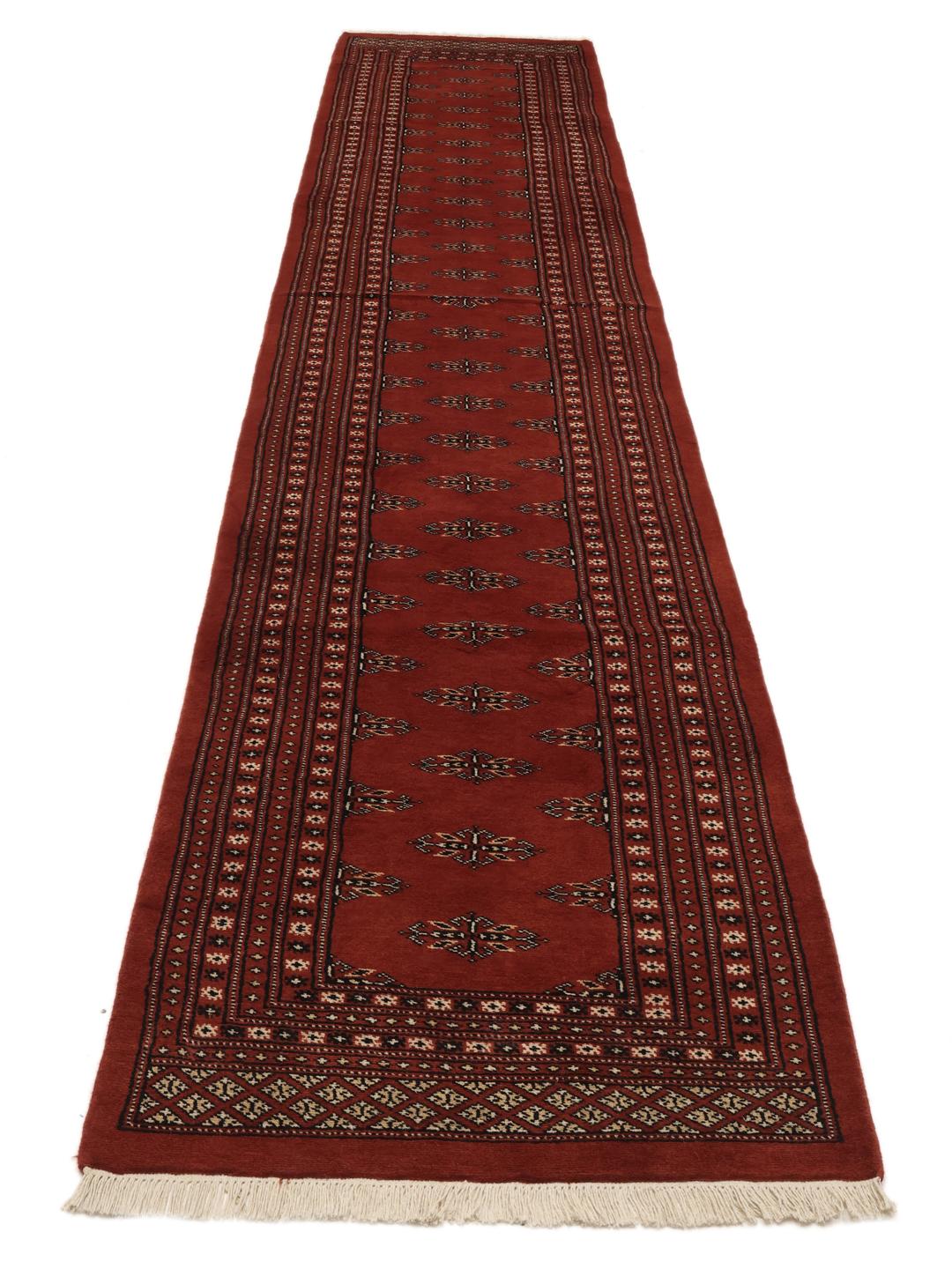 En lang, håndknyttet løber fra Pakistan med en dybrød bund og gentagne geometriske motiver.