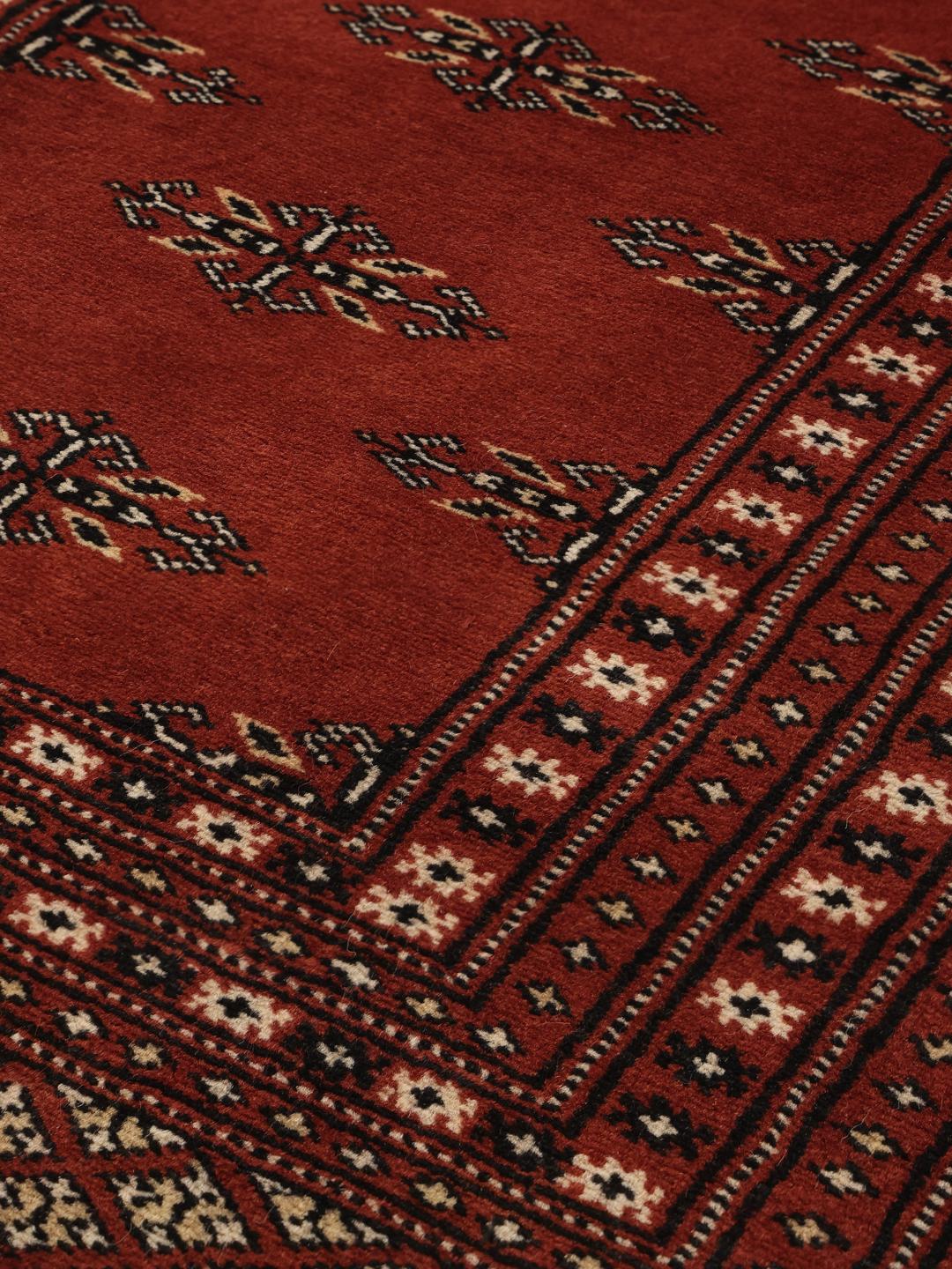 En lang, håndknyttet løber fra Pakistan med en dybrød bund og gentagne geometriske motiver.