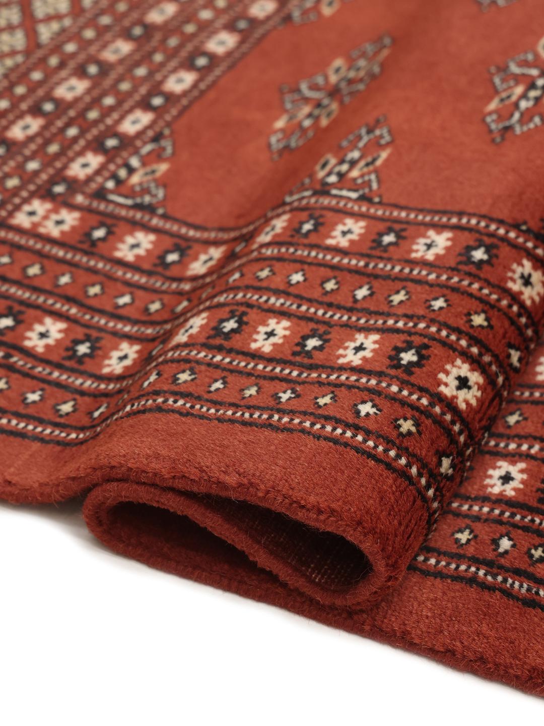 En lang, håndknyttet løber fra Pakistan med en dybrød bund og gentagne geometriske motiver.