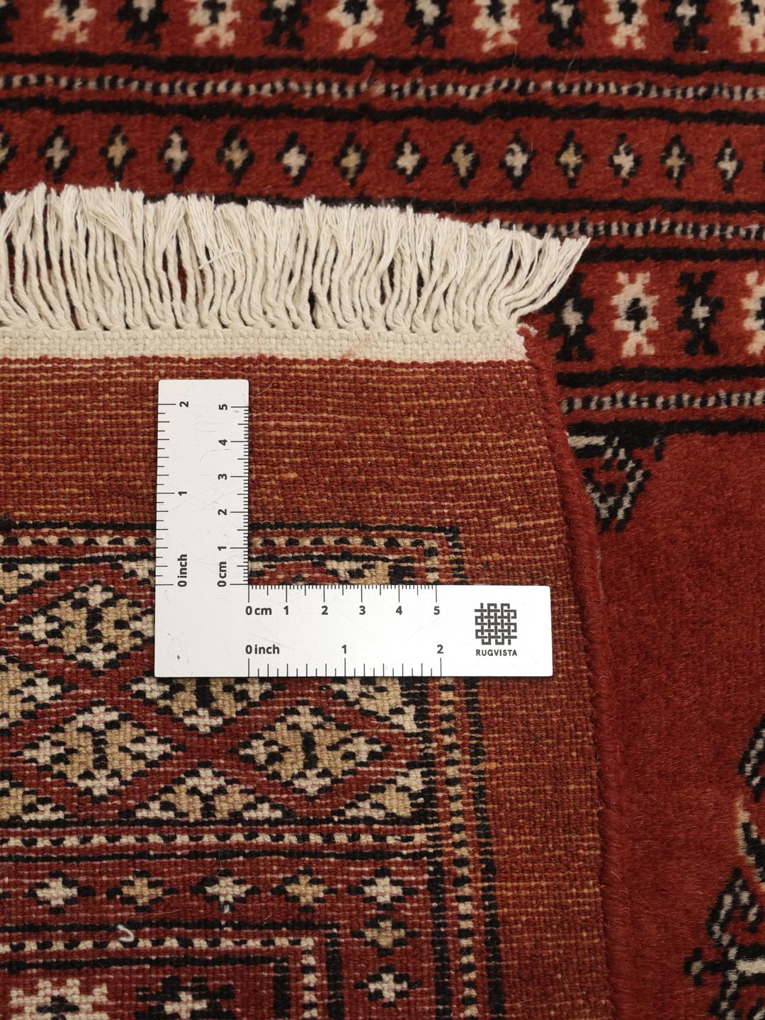 En lang, håndknyttet løber fra Pakistan med en dybrød bund og gentagne geometriske motiver.