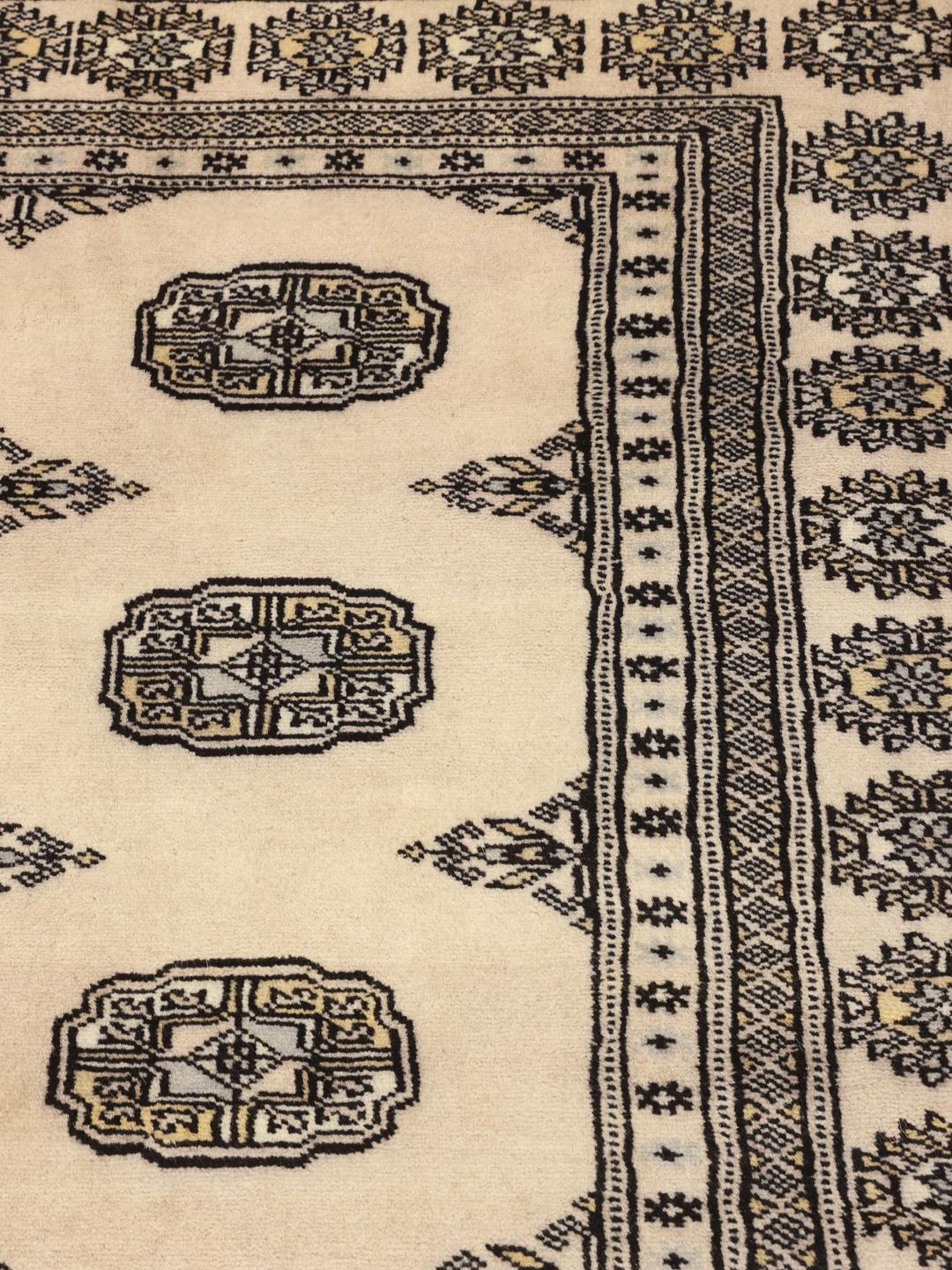 Een vierkant, handgeknoopt Pakistan Bokhara tapijt in beige wol met donkere geometrische motieven.