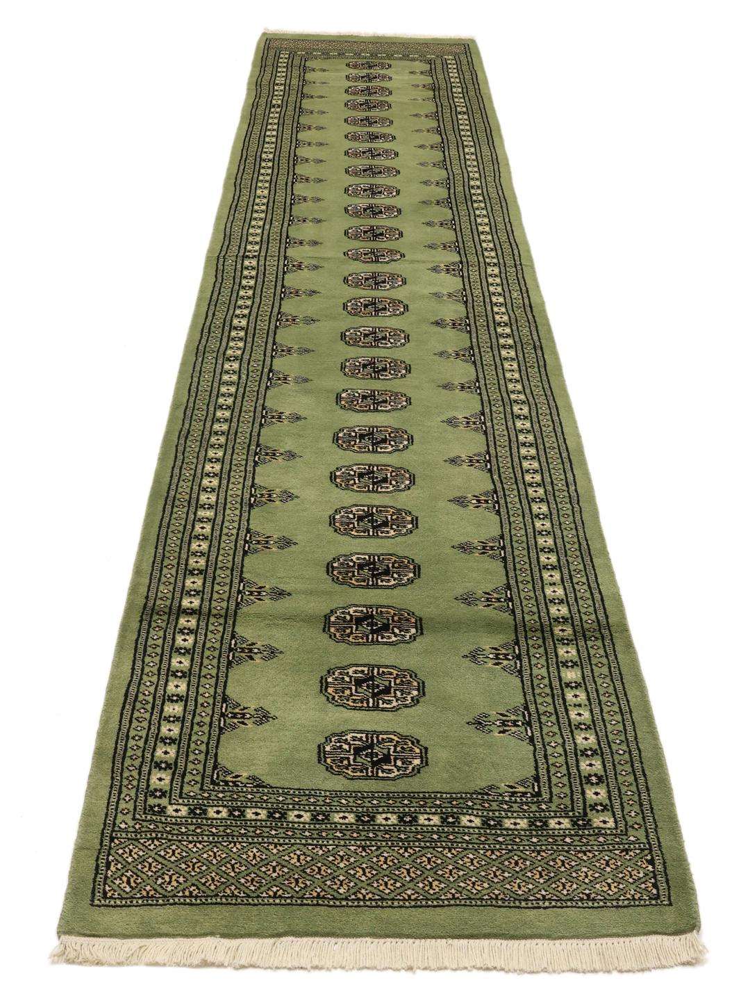 A long, hand-knotted runner from Pakistan with a green field and traditional patterns.