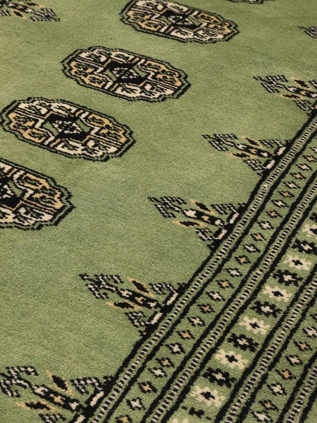 A long, hand-knotted runner from Pakistan with a green field and traditional patterns.