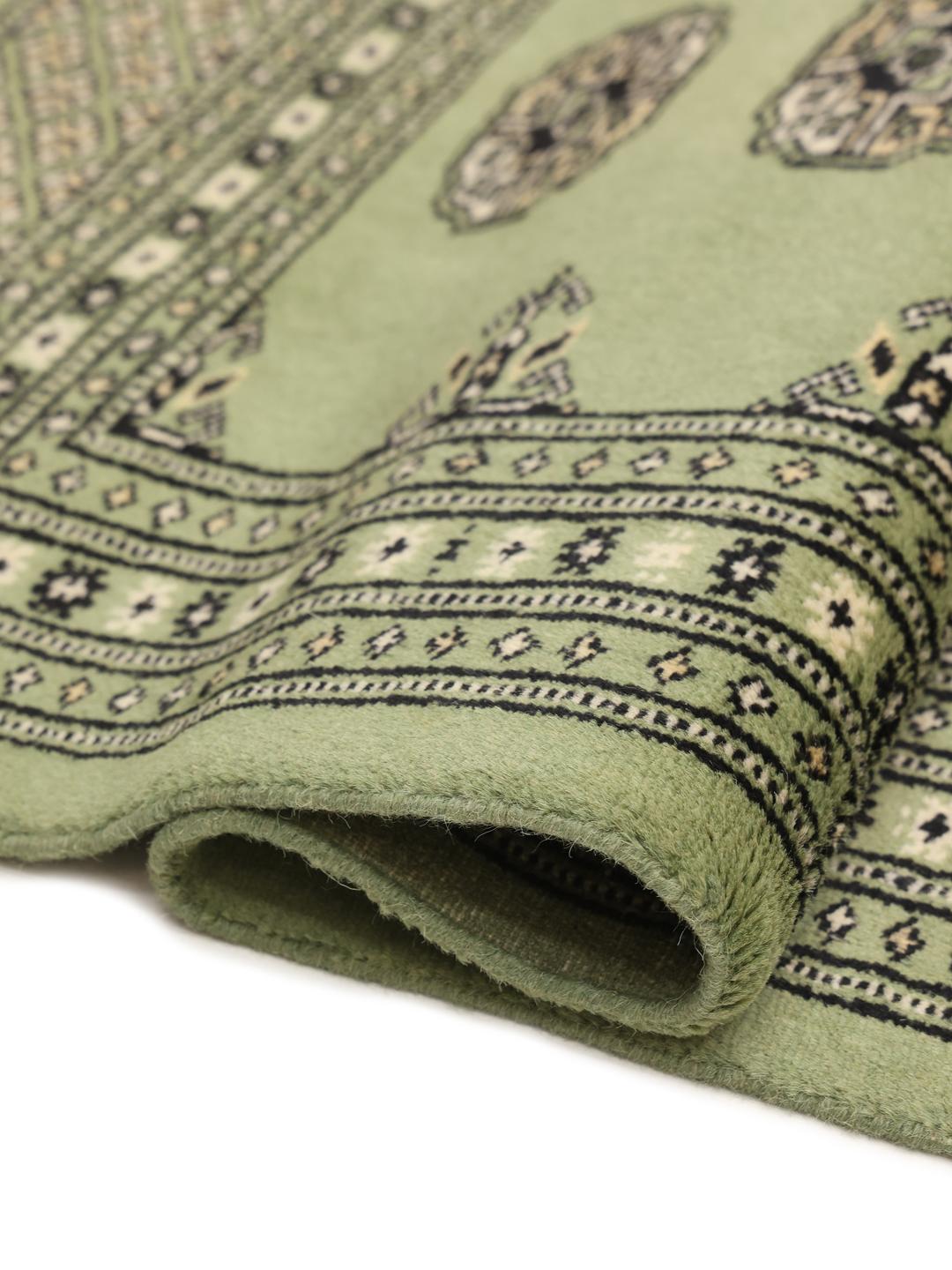 A long, hand-knotted runner from Pakistan with a green field and traditional patterns.