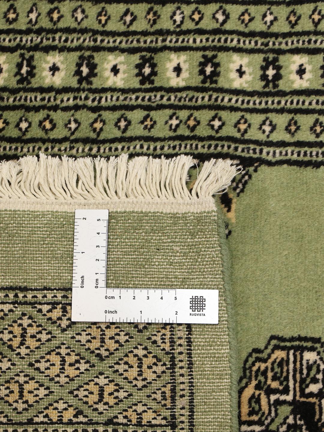 A long, hand-knotted runner from Pakistan with a green field and traditional patterns.