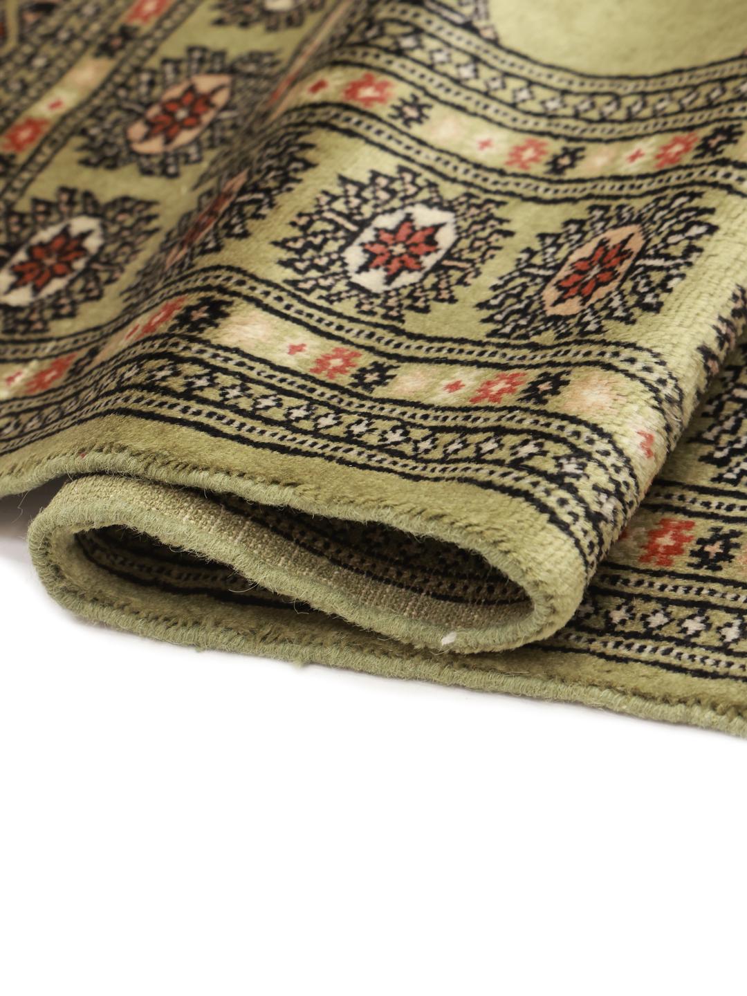 A hand-knotted Pakistan Bokhara rug with a green field and traditional motifs