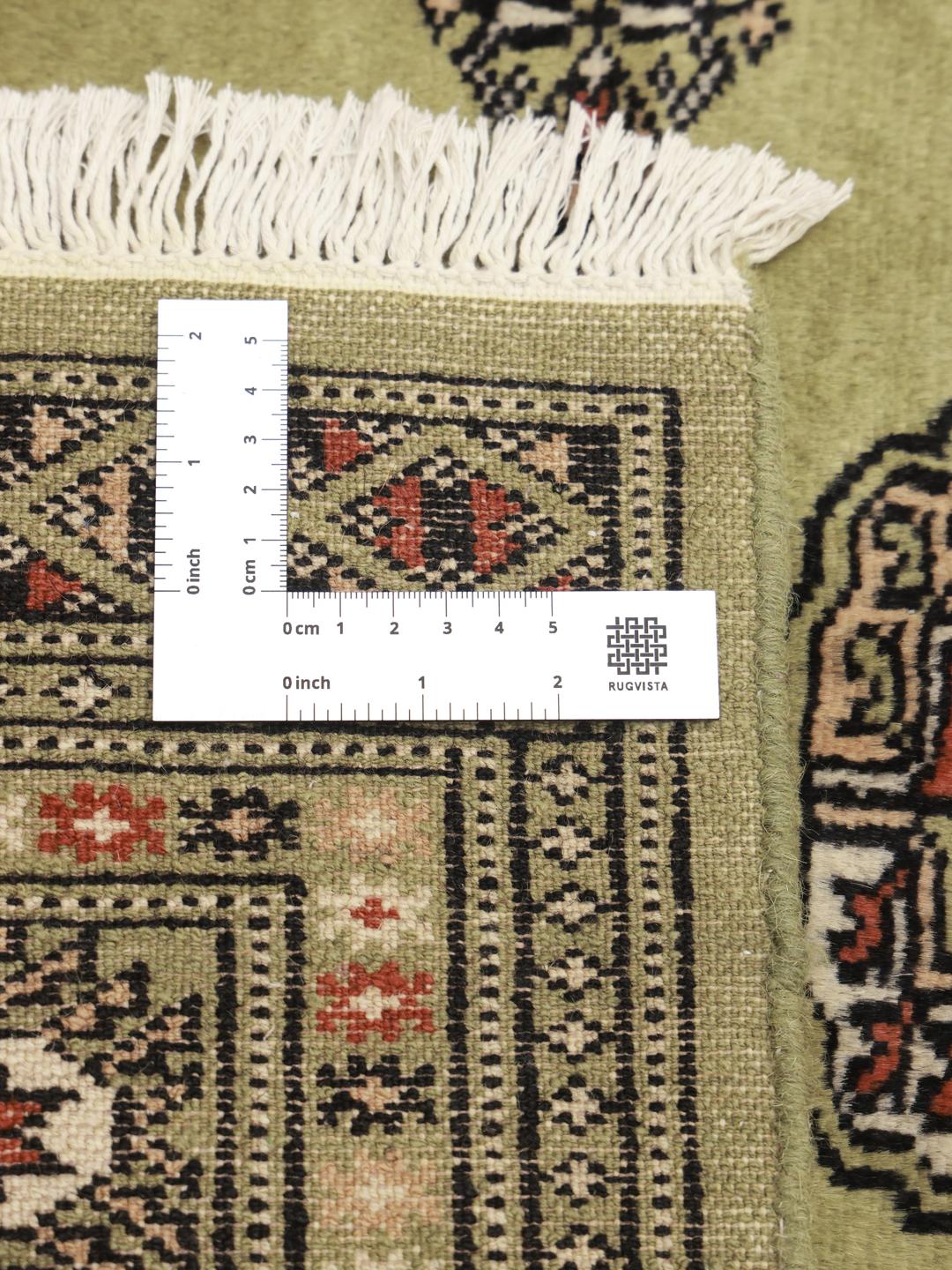 A hand-knotted Pakistan Bokhara rug with a green field and traditional motifs