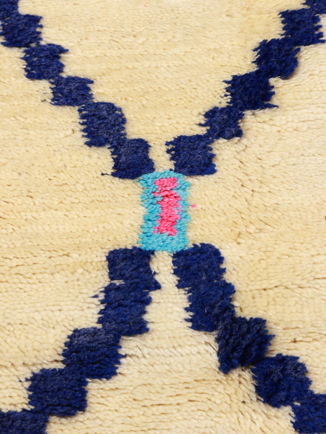 Een met de hand geknoopt Berber Marokkaans tapijt met een geometrisch ruitpatroon in blauw en zwart op een beige wollen achtergrond.