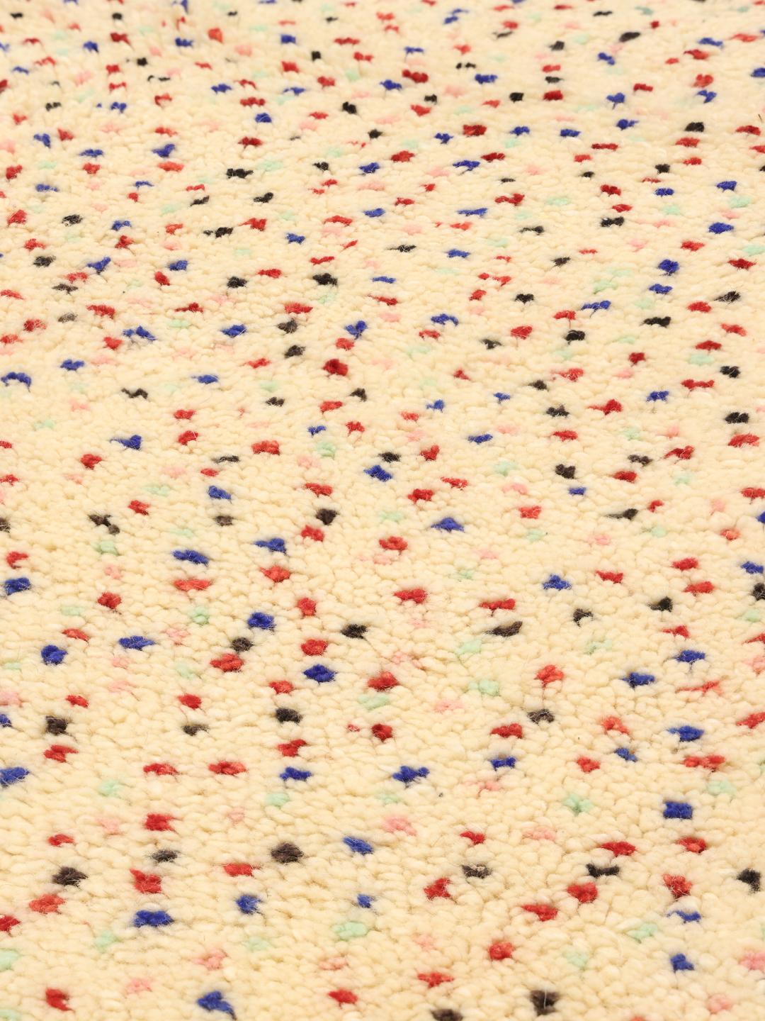 Handgemaakt Berber Marokkaans tapijt met meerkleurige spikkels op een beige achtergrond.