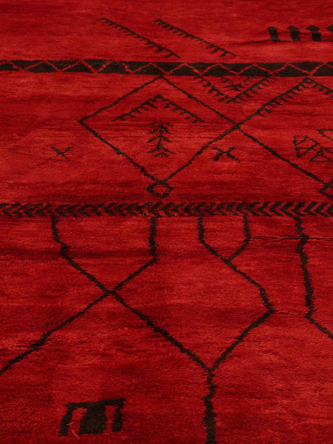 Een groot handgeknoopt Marokkaans tapijt met een levendig rood veld en donkere geometrische patronen.