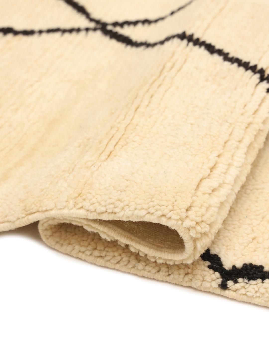 Håndknyttet marokkansk tæppe med diamantmønstre i beige og sort.