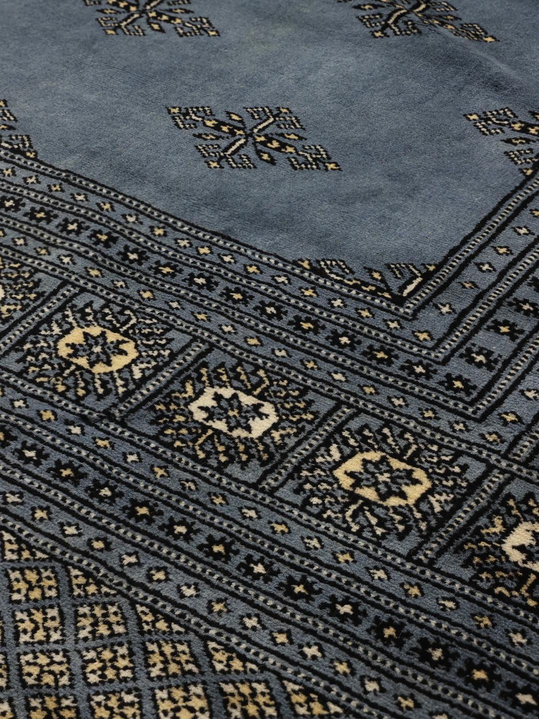 A hand knotted Bokhara rug from Pakistan in a soft blue color with intricate repeating motifs.