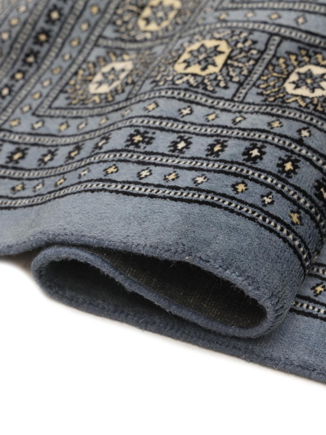 A hand knotted Bokhara rug from Pakistan in a soft blue color with intricate repeating motifs.