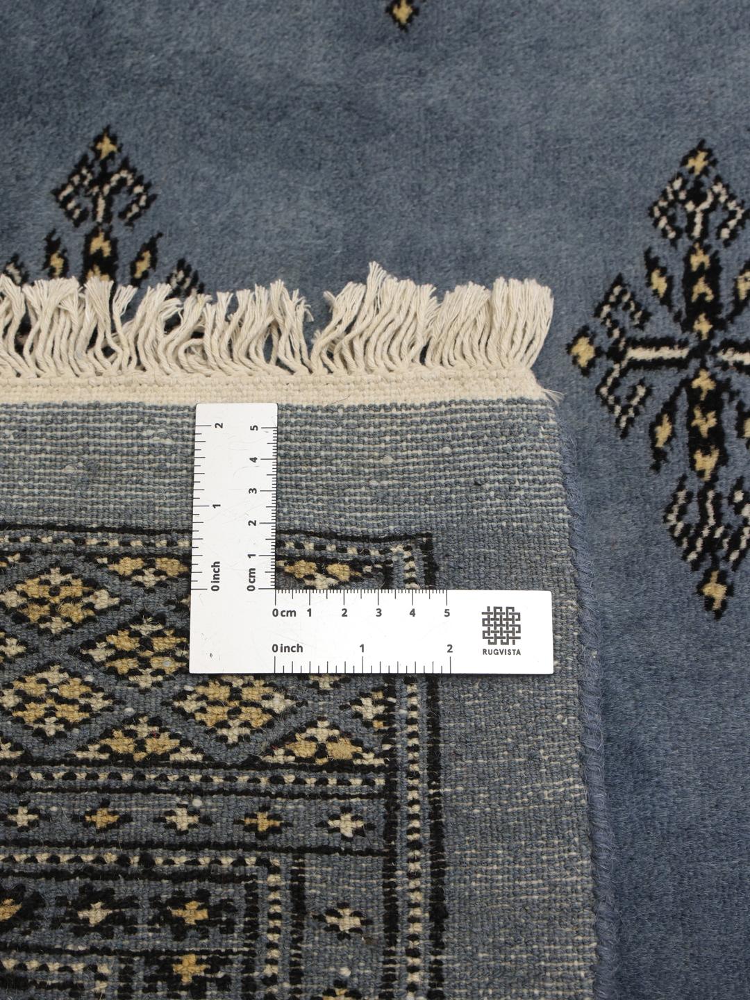 A hand knotted Bokhara rug from Pakistan in a soft blue color with intricate repeating motifs.