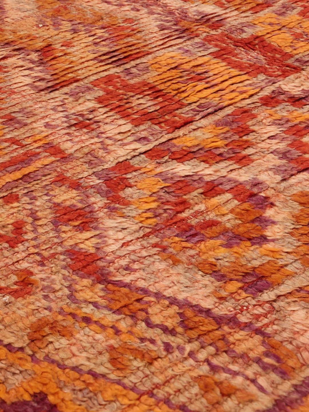 En vintage marokkansk løber med komplekse geometriske mønstre i nuancer af rød og orange.