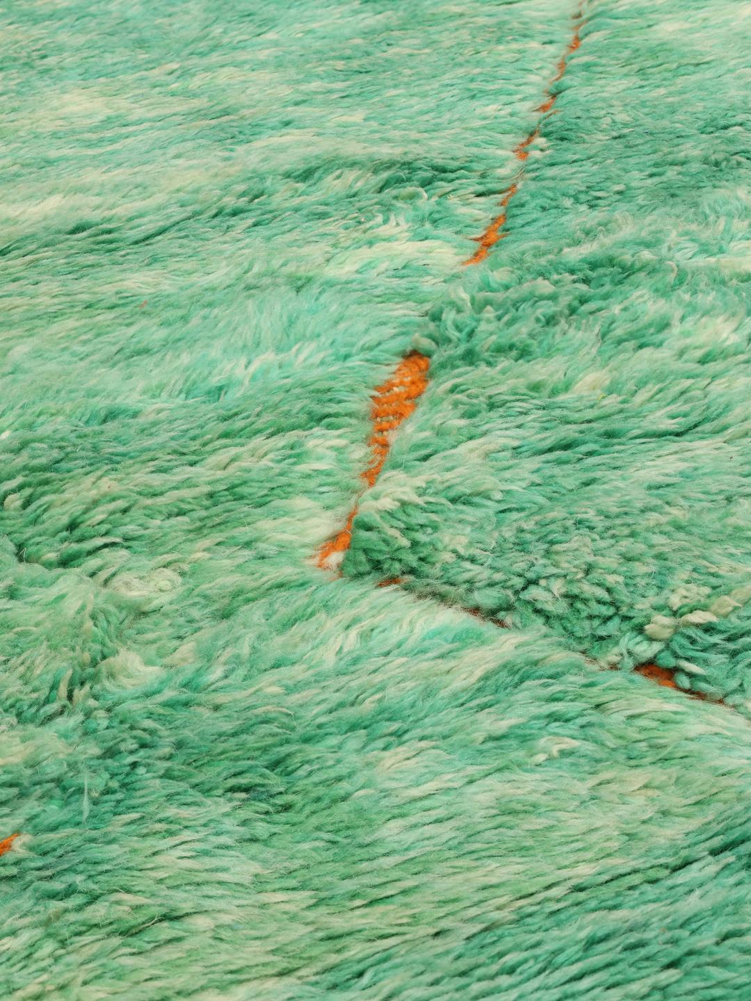 Een groot rechthoekig handgeknoopt Marokkaans tapijt met een levendig groen veld en oranje ruitpatronen.