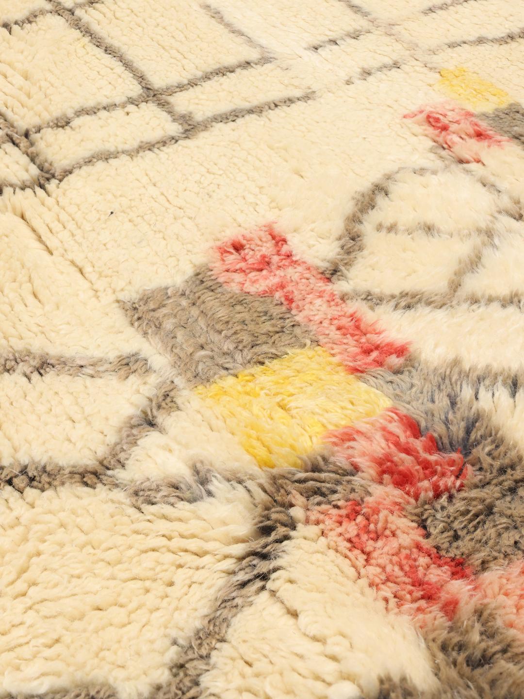 Un tapis marocain noué à la main avec un fond crème et des motifs géométriques multicolores.