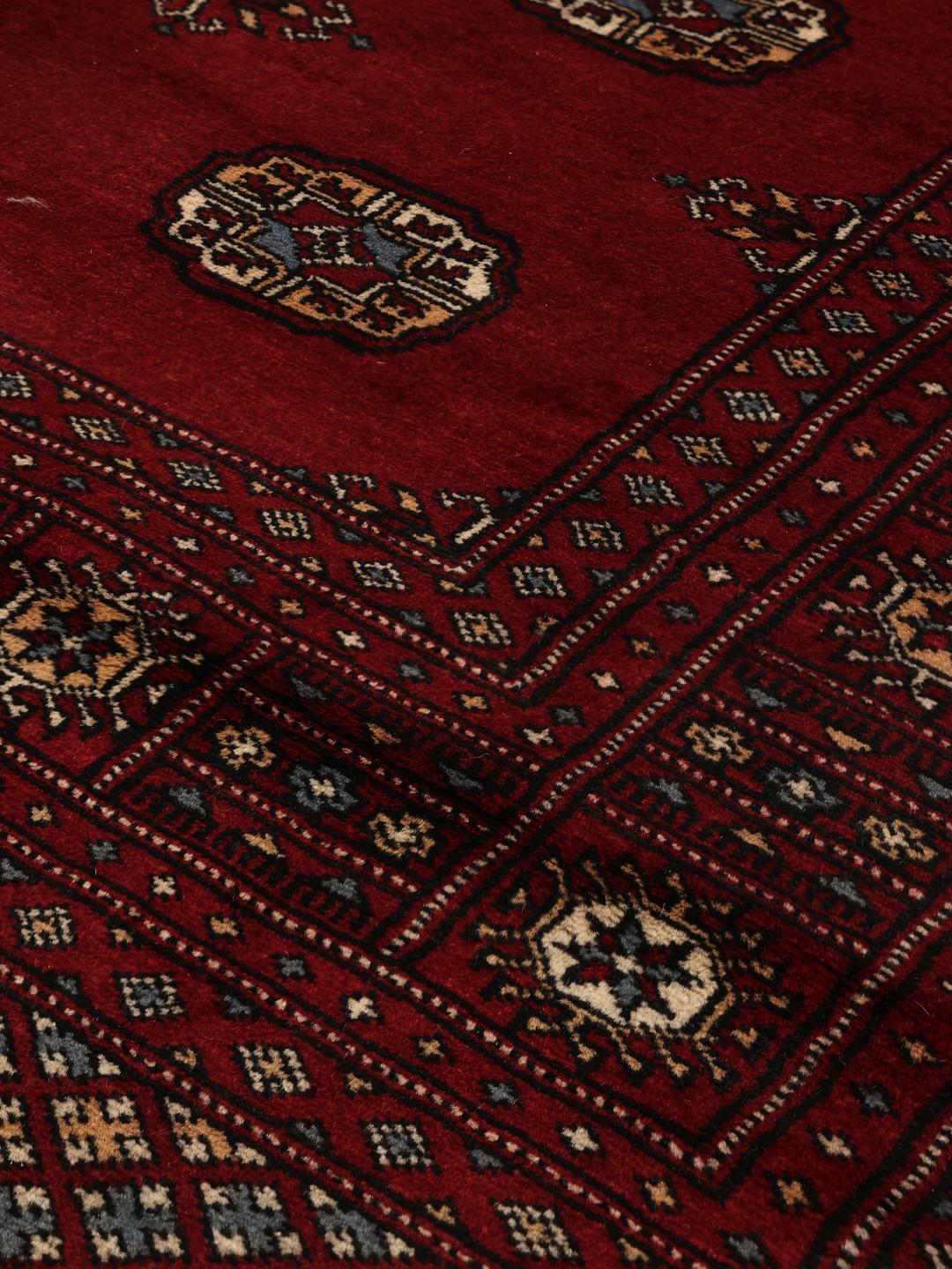 Hand-knotted Pakistani Bokhara rug in a deep red tone with traditional geometric patterns