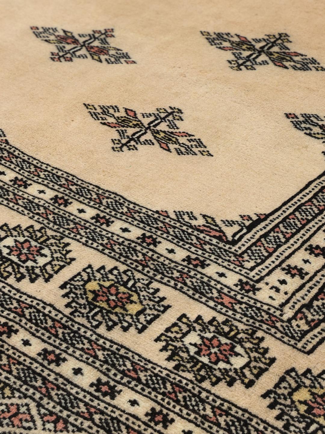 Un tapis Bokhara carré originaire du Pakistan avec un champ beige clair et des motifs floraux répétitifs.