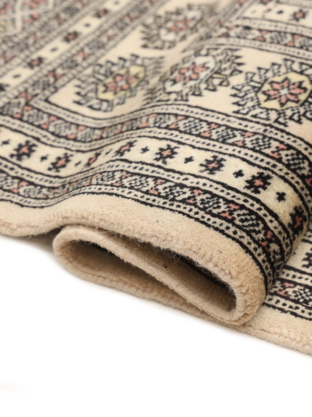 Un tapis Bokhara carré originaire du Pakistan avec un champ beige clair et des motifs floraux répétitifs.