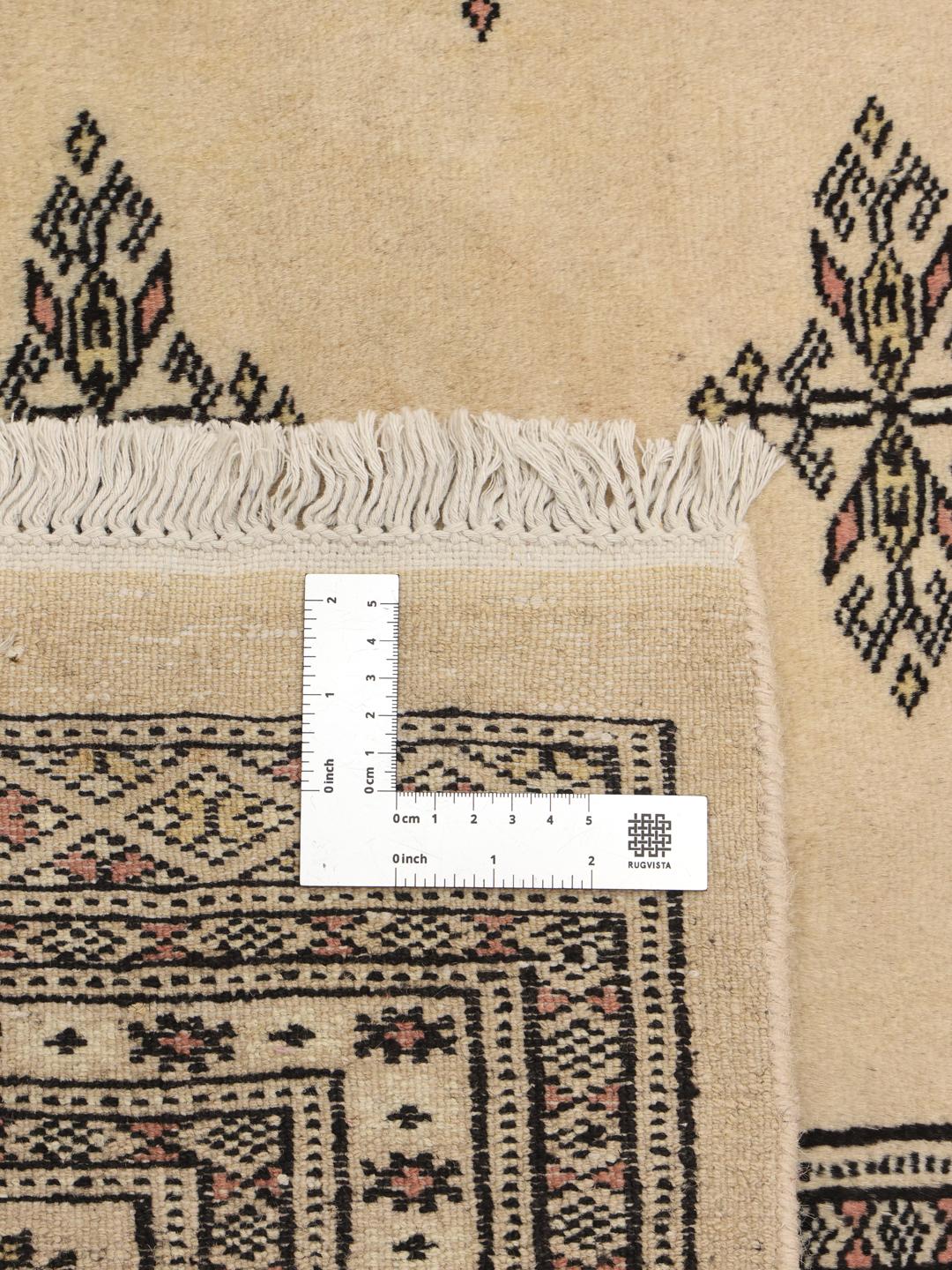 Un tapis Bokhara carré originaire du Pakistan avec un champ beige clair et des motifs floraux répétitifs.