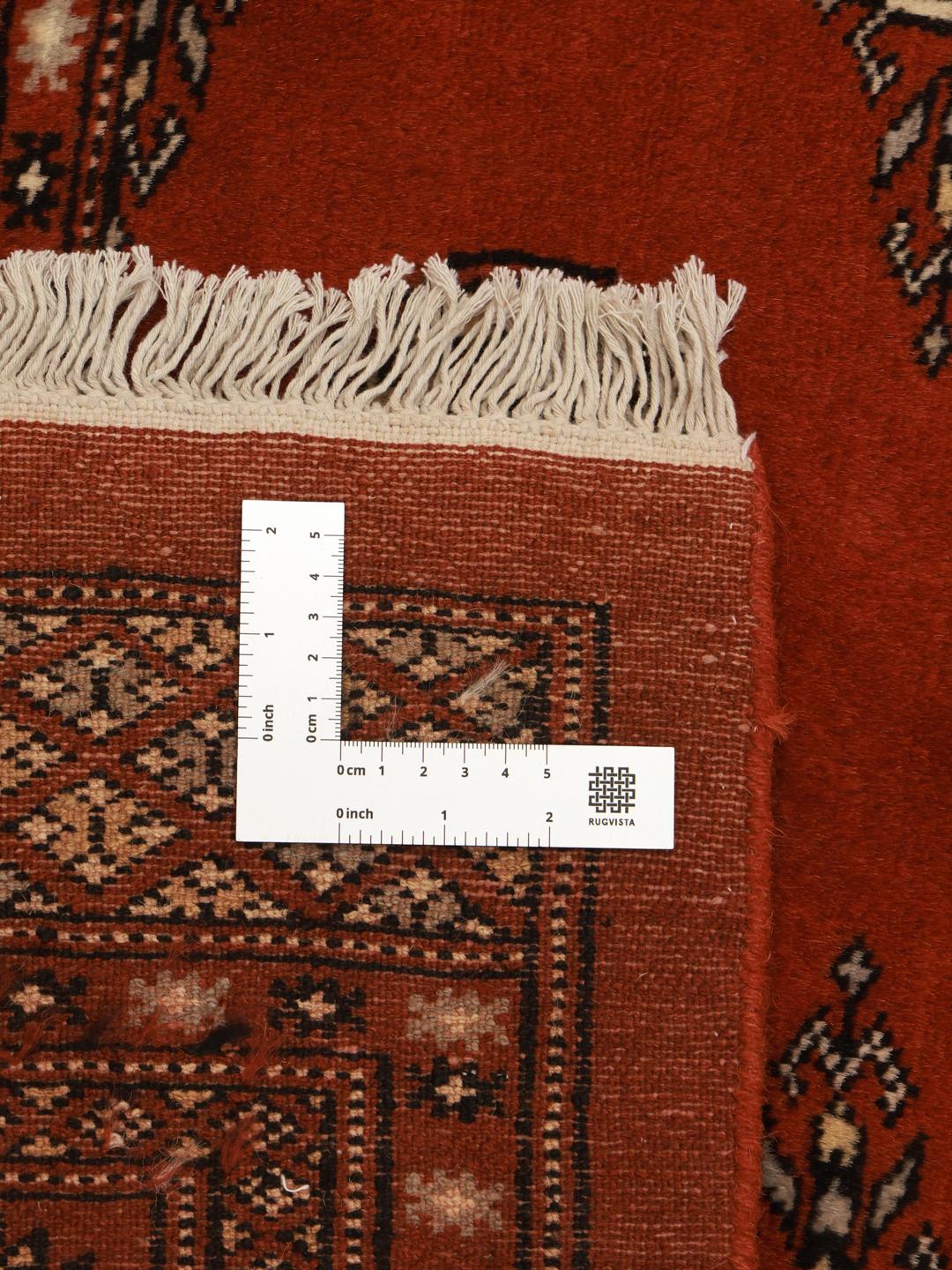 Et firkantet håndknyttet Bokhara tæppe fra Pakistan i dyb rød med geometriske motiver.