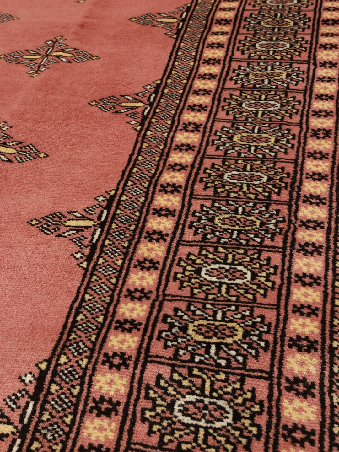Een rechthoekig handgeknoopt Bokhara-tapijt uit Pakistan met een roze veld en geometrische patronen.