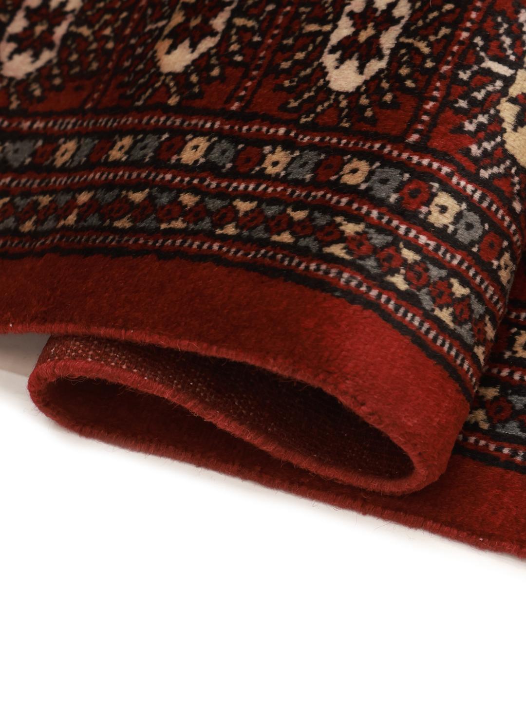 Een vierkant, dieprood handgeknoopt Bokhara tapijt uit Pakistan met traditionele herhalende motieven.