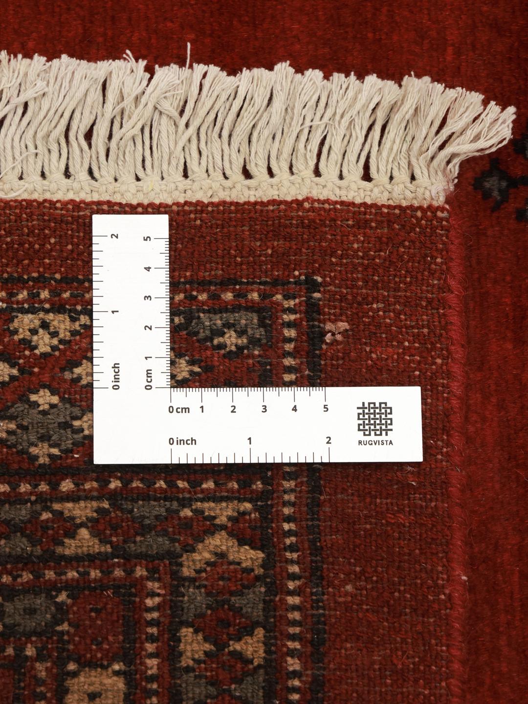 Een vierkant, dieprood handgeknoopt Bokhara tapijt uit Pakistan met traditionele herhalende motieven.