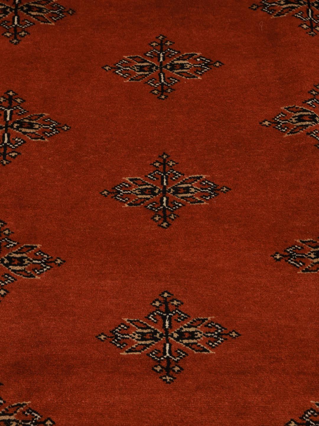 Een vierkant handgeknoopt Bokhara tapijt uit Pakistan met een dieprood veld en geometrische motieven.