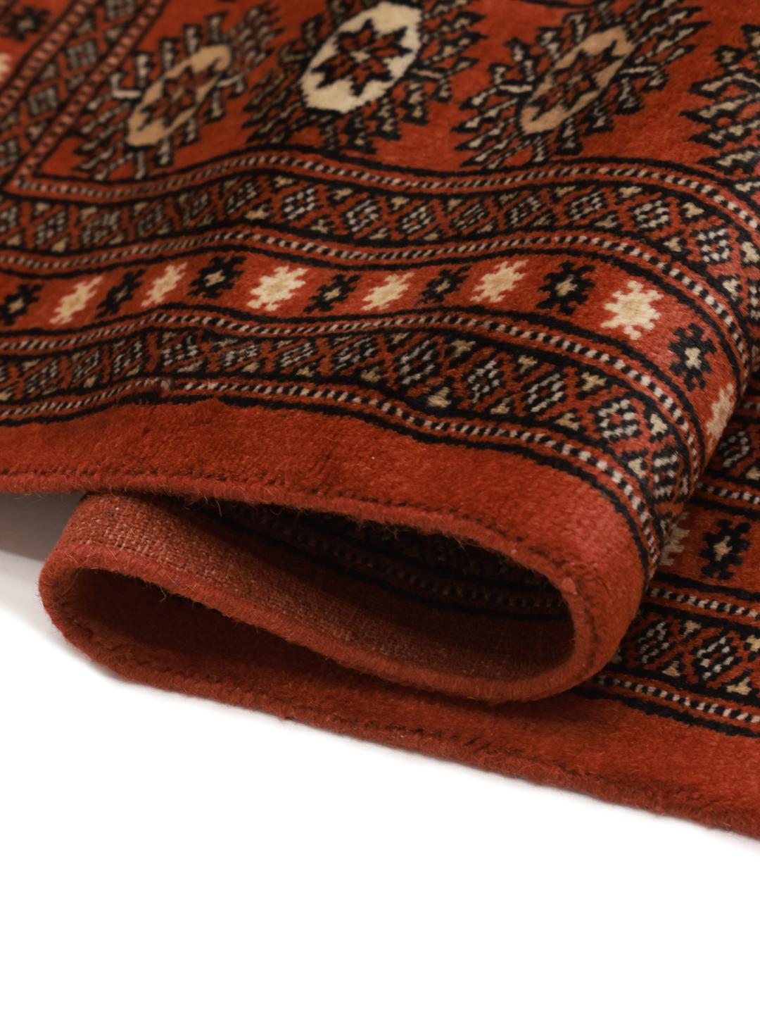 Een vierkant handgeknoopt Bokhara tapijt uit Pakistan met een dieprood veld en geometrische motieven.