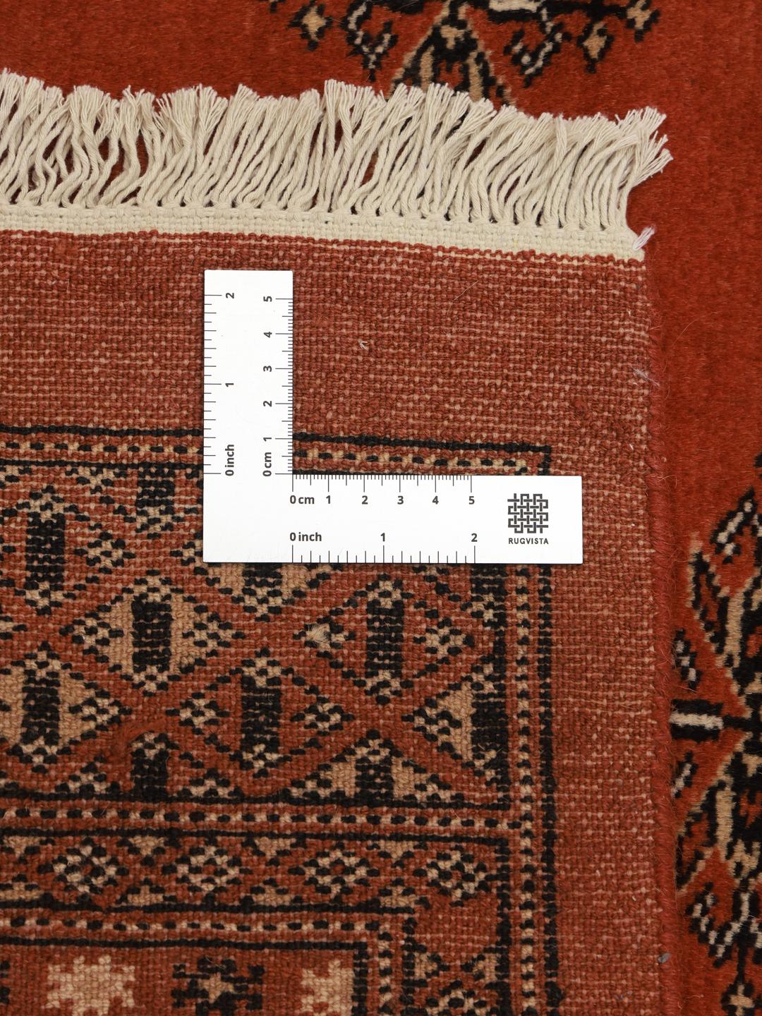 Een vierkant handgeknoopt Bokhara tapijt uit Pakistan met een dieprood veld en geometrische motieven.