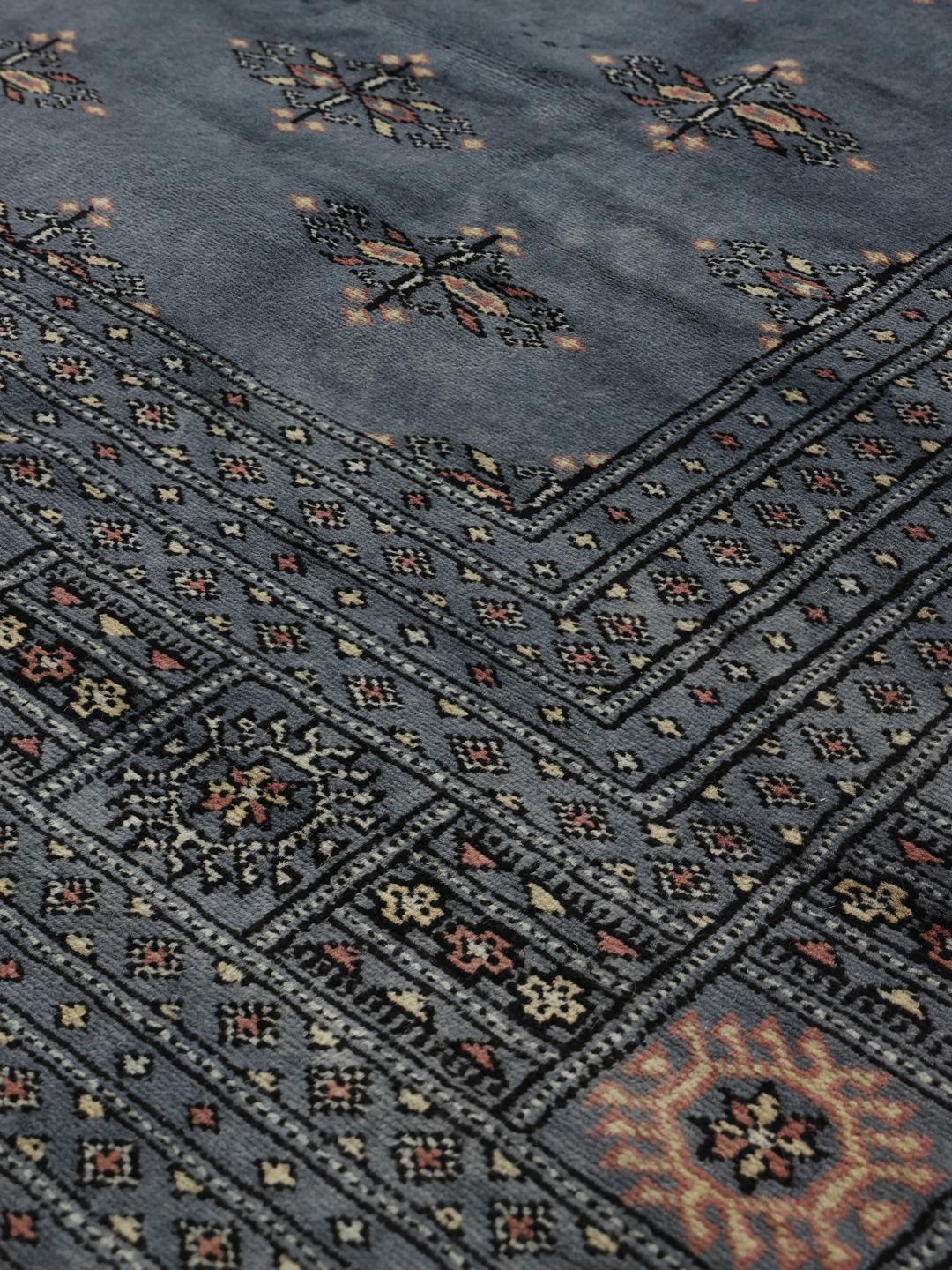 Et stort håndknyttet blåt pakistansk tæppe med gentagne geometriske motiver og en dekorativ kant.