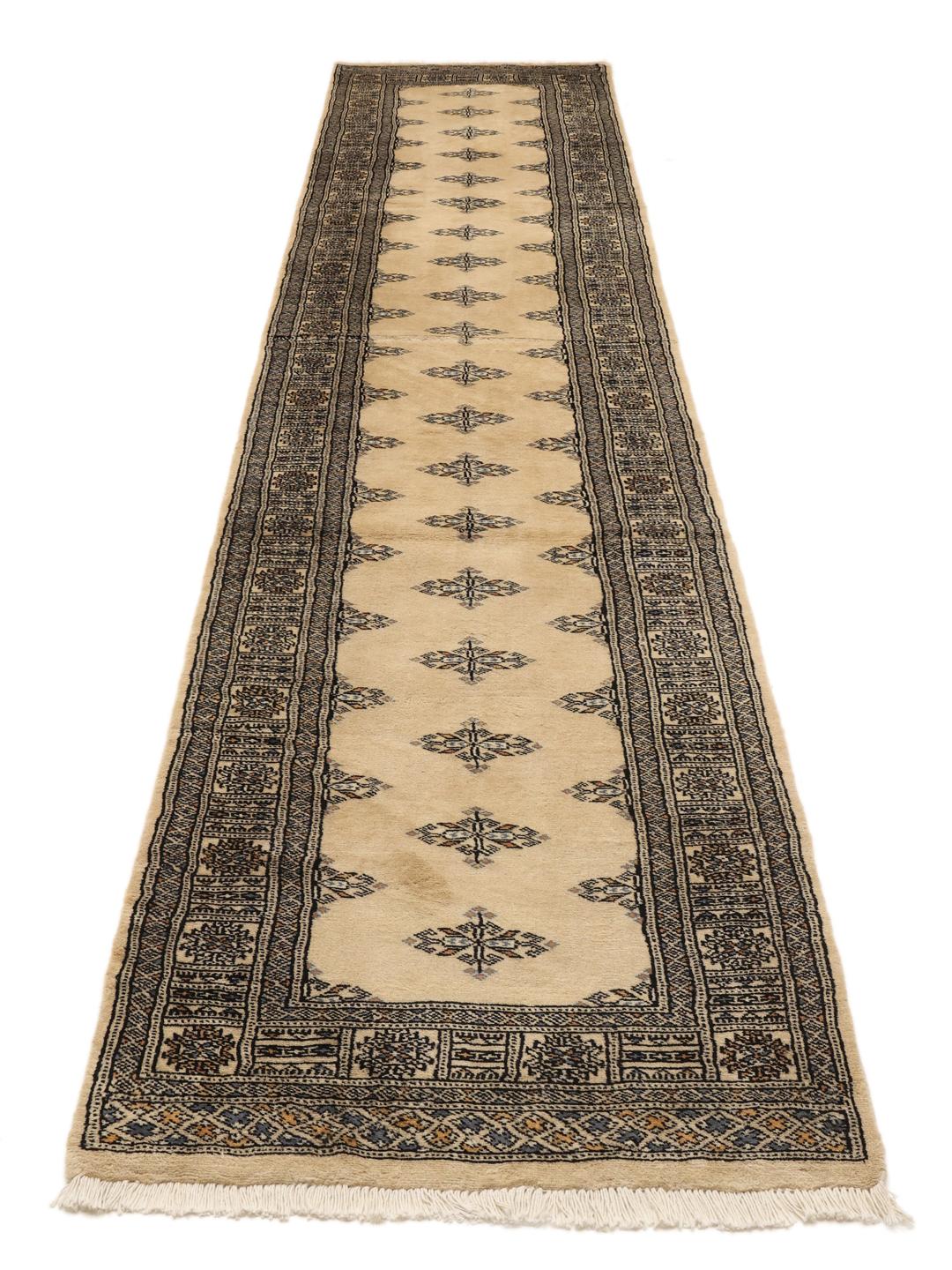 A long, cream-colored Pakistani hand-knotted runner with dark geometric motifs.