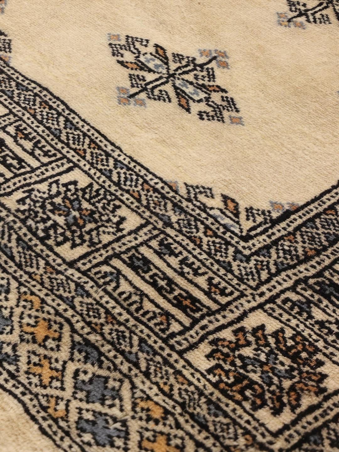 A long, cream-colored Pakistani hand-knotted runner with dark geometric motifs.