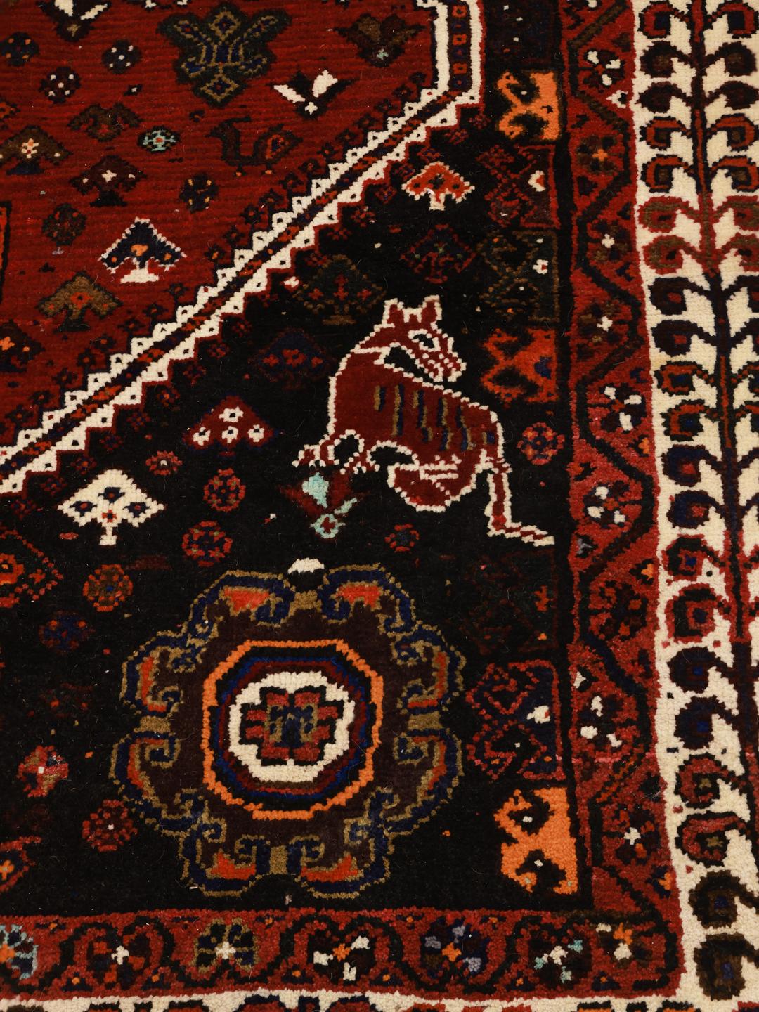 A hand-knotted Shiraz rug from the Middle East featuring a vibrant red and black geometric design.