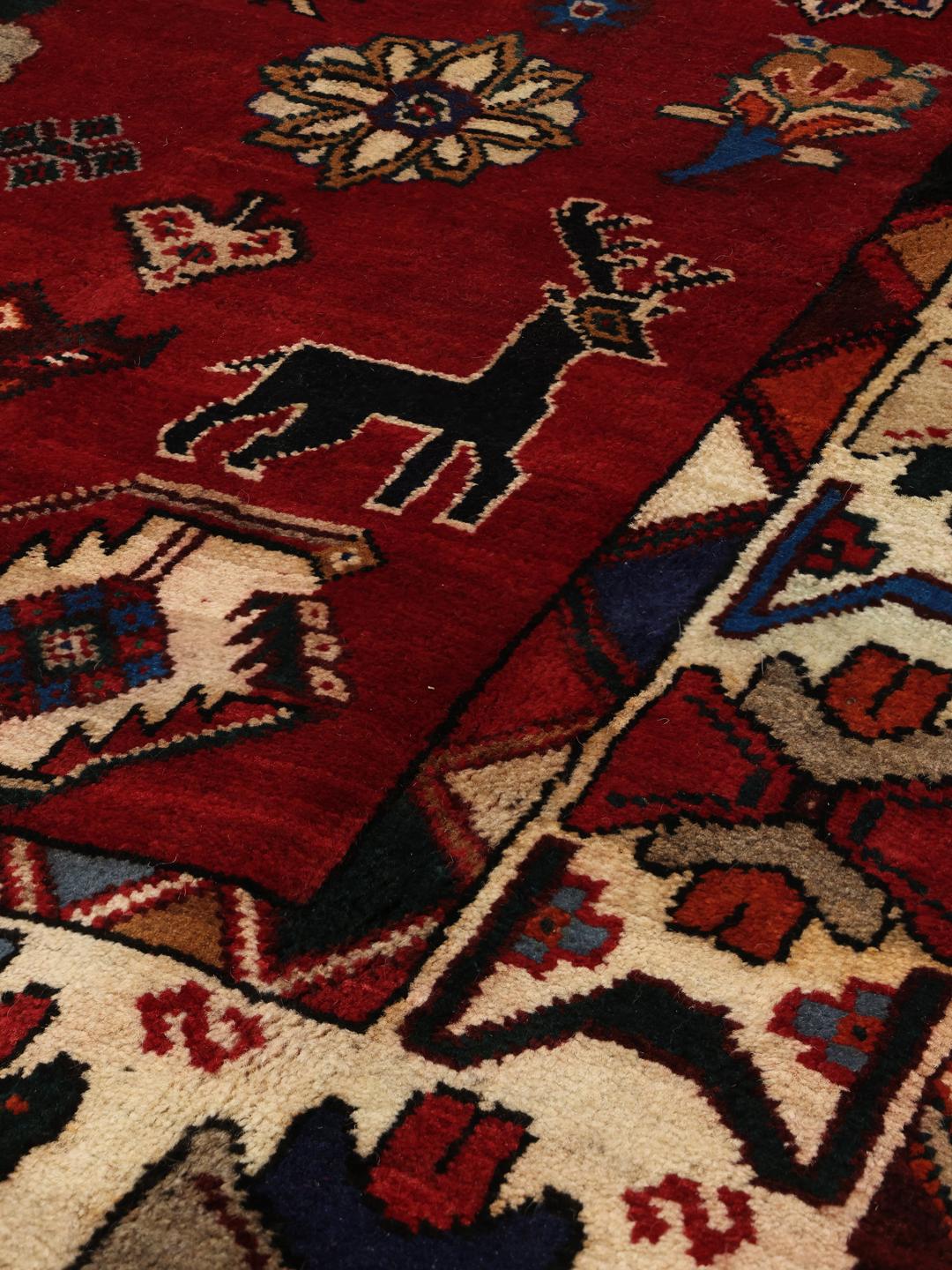 A hand-knotted Ghashghai rug from the Middle East featuring a vibrant red field with intricate geometric motifs.