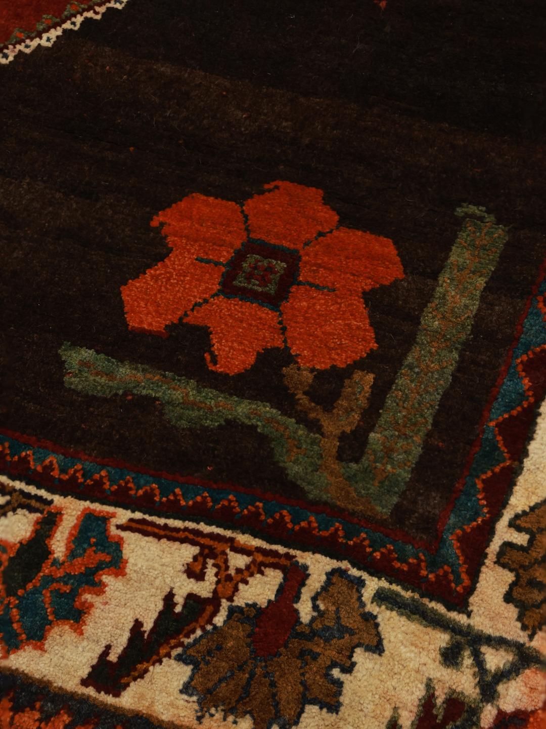 A hand-knotted Shiraz rug from the Middle East featuring a dark red field with floral motifs in a vibrant, decorative style.