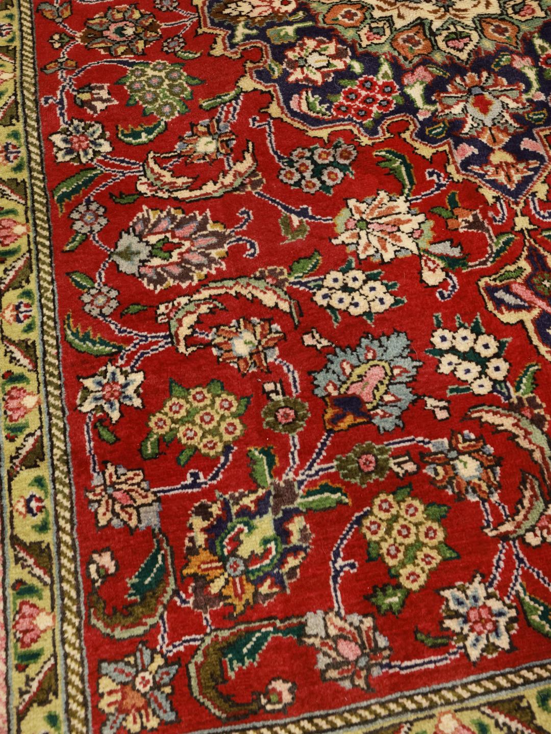 A hand-knotted Tabriz rug from the Middle East featuring a vibrant red field with a blue central medallion.