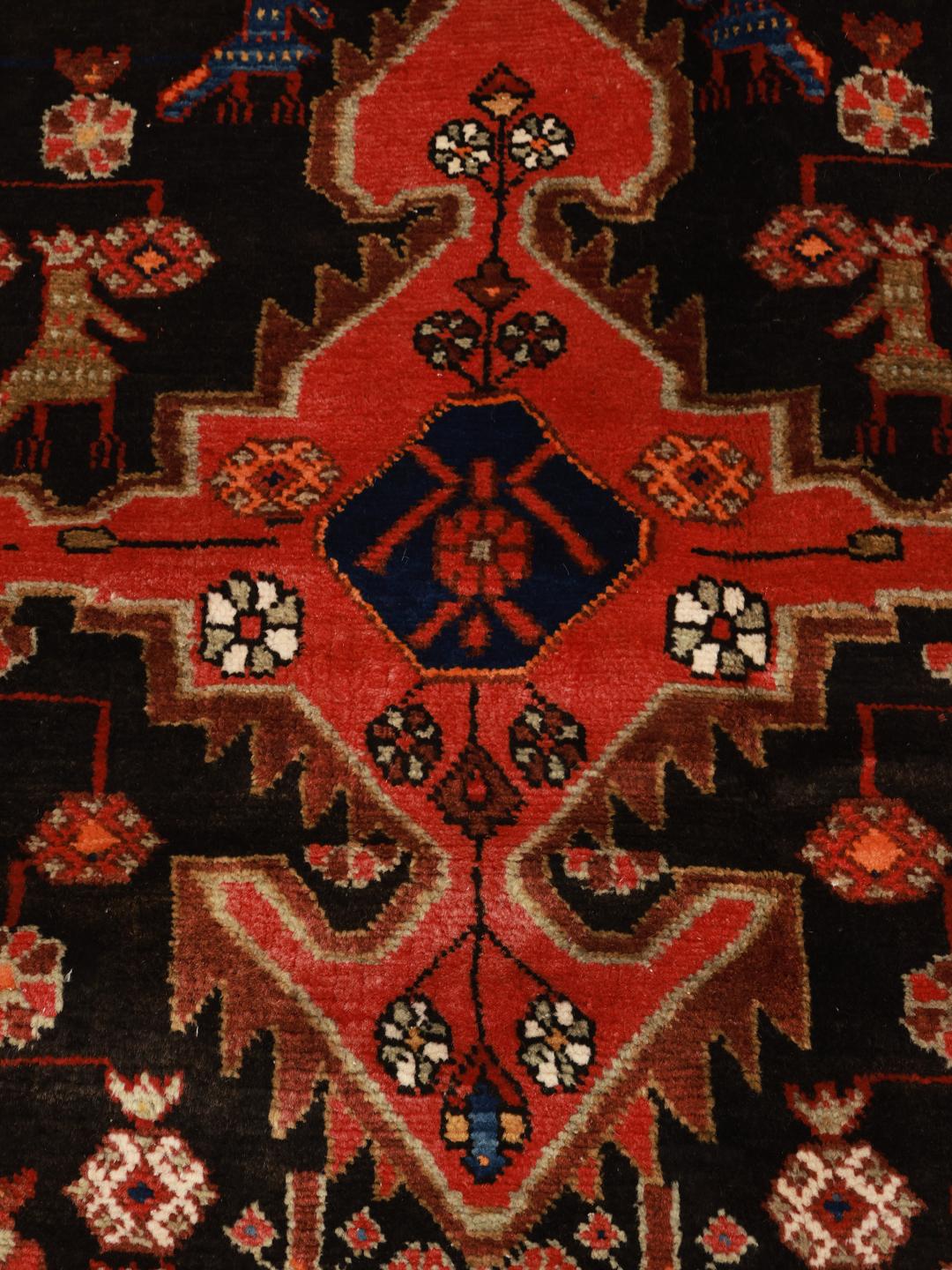 Et håndknyttet Nahavand-tæppe fra Mellemøsten med en rød og sort farvepalette og traditionelle dyre- og blomstermotiver.