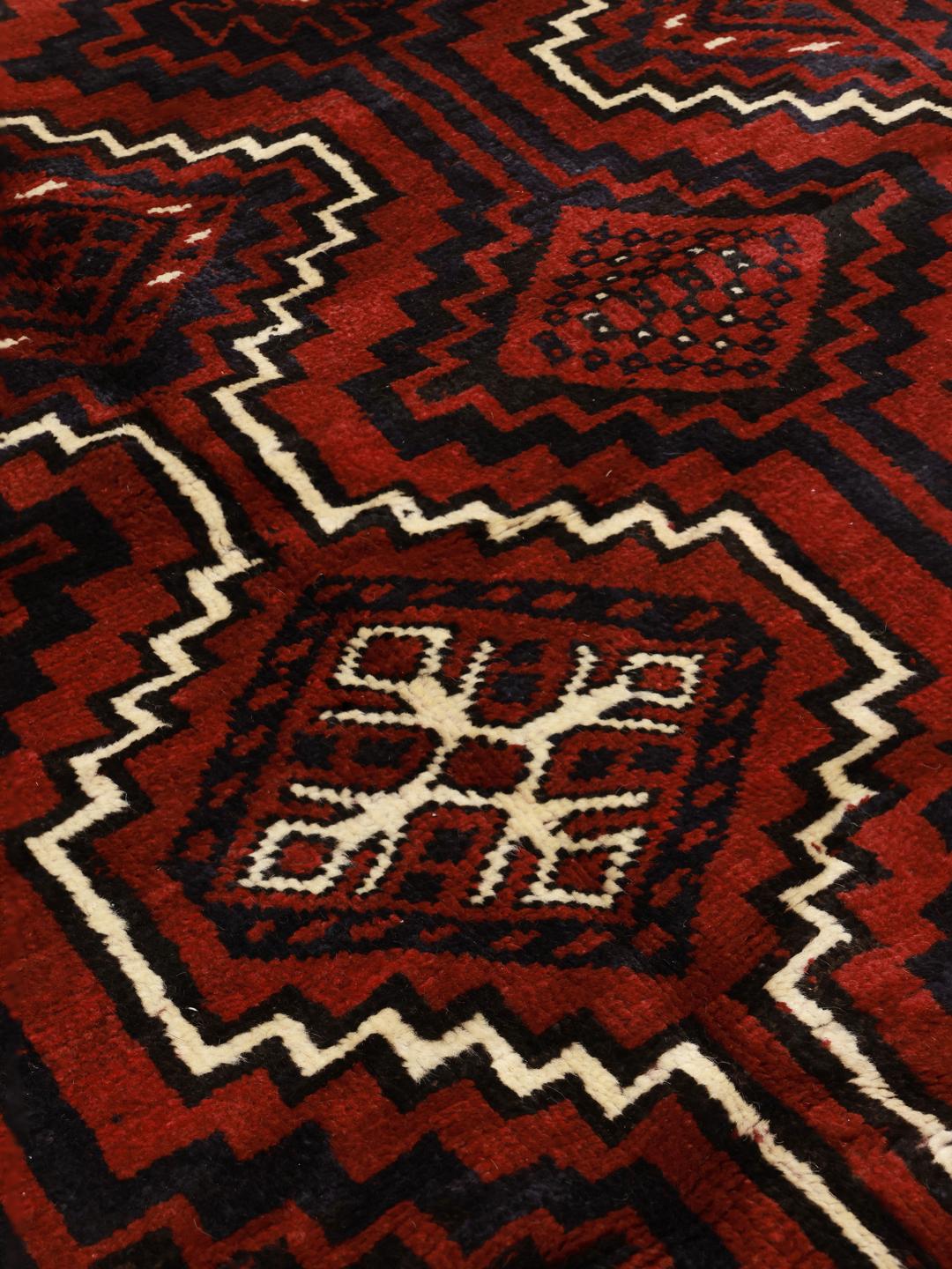 A hand-knotted Lori rug from the Middle East with a deep red and geometric pattern.