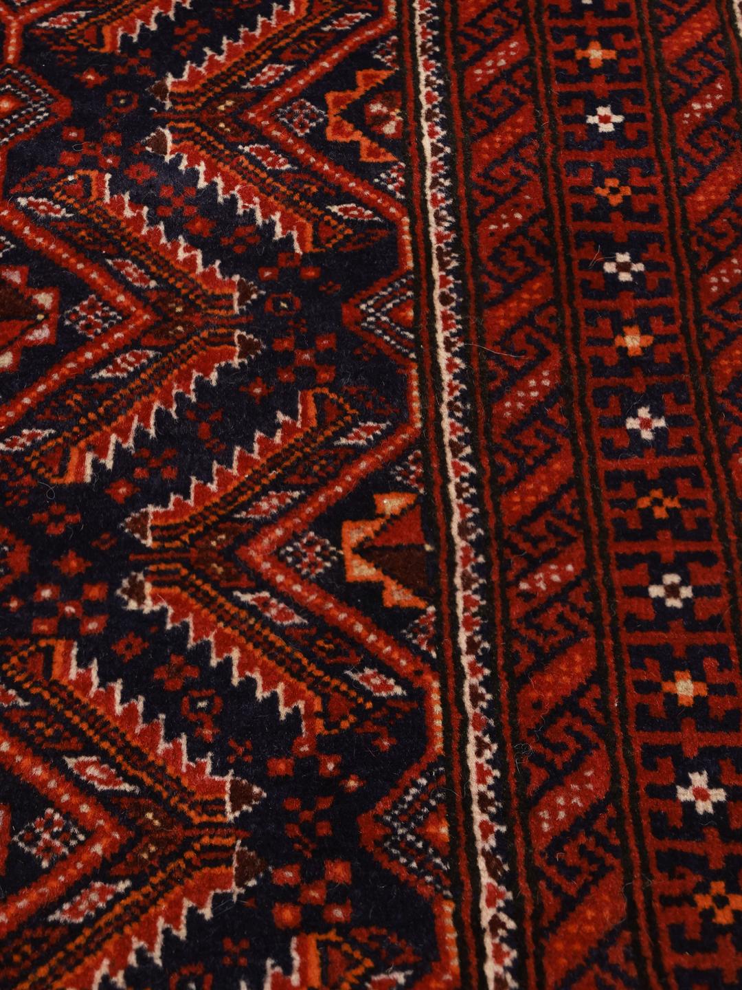 Een handgeknoopt Beluch tapijt met verfijnde geometrische patronen in donkerrode en blauwe tinten.